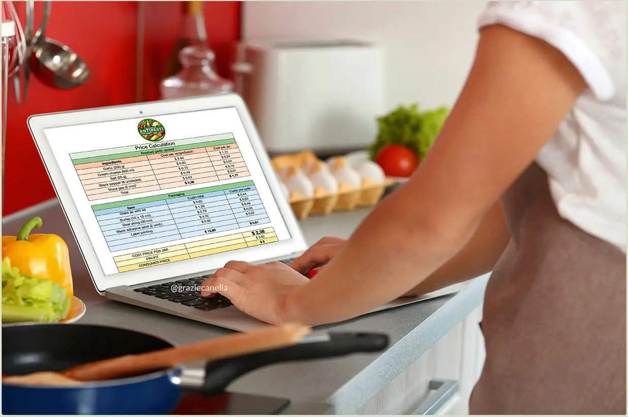 Person typing cost spreadsheet for antipasti production on a kitchen laptop.